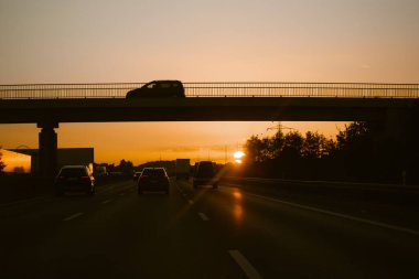 Madrid, Spain. 1 May 2021 Cars on highway at sunset sunlight. A rapid movement of cars, truckers trucks on a road going into a distance at dawn. Bridge over a freeway roadway. Travel, rip on a car.