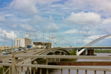 Köprünün panorama manzarası ve yüksek hızlı araba trafiği. Rüzgarlı bir yaz gününde mavi bulutlu bir gökyüzüne karşı sokak lambaları. Yol aydınlatma. Gündüz vakti şehrin ışık direkleri. Şehir manzarası. Kyiv, Ukrayna.