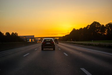Madrid, Spain. 1 May 2021 Cars on highway at sunset sunlight. A rapid movement of cars, truckers trucks on a road going into a distance at dawn. Freeway roadway in the evening. Travel, trip on a car.