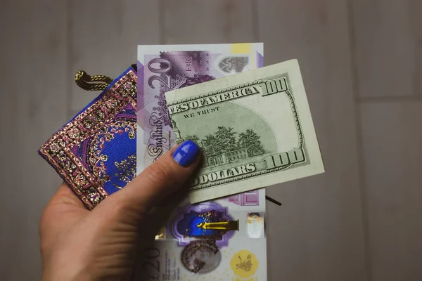 London, UK. May 1, 2022 New bill of 20 British pounds GBP and 100 U.S. dollars USD in a blue woman's purse in hands. Economy, finance, spending, shopping, investments, saving money concept. Cash.