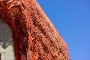 Protective net. Reconstruction of facade of historic classical apartment building on city street. Red facade construction mesh covers an old house closed for renovation exterior. Construction site. 