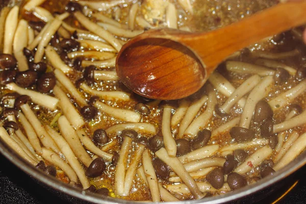The process of cooking mushrooms in a pan brown shimiji or shimeji mushrooms selective focus. Hypsizygus tessulatus native to East Asia. Vegetarian vegan healthy food cook. Beech mushroom roasting.