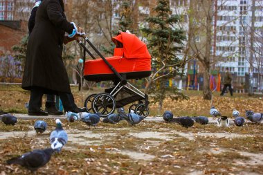 Faceless woman with red stroller walking with infant on city street on cold fall or winter day. Motherhood, childcare, parenthood concept. A mother outdoors with a little newborn kid toddler baby. 