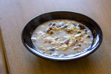 Oatmeal or granola with milk and dried fruit, raisins in a black bowl on a wooden table top view selective focus. Healthy, wholesome breakfast food at home, cafe. Vegetarian Meals, nutrition for diet.