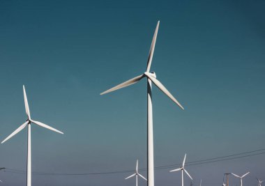 Mavi gökyüzüne karşı yel değirmenleri. Yenilenebilir enerji üretimi, ekoloji, alternatif elektrik kavramı. Yeşil teknoloji. Beyaz pervaneli rüzgâr çiftliği. Rüzgar değirmeni endüstrisi. Güç ve enerji.