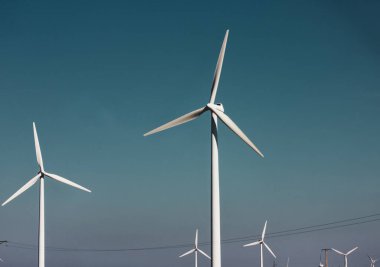 Windmills against a dramatic blue sky. Renewable energy production, ecology, alternative electricity concept. Green technology. Windfarm with white propellers. Wind mills industry. Power and energy. clipart