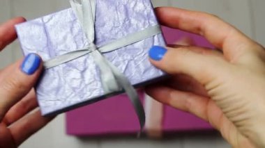 Purple gift box with silver silk bow in woman's hand on gray background. Gift giving. Shopping, shopping, gifts to loved ones concept. Gifts in a box for the lovers, mother, daughter, girl Boxing gift