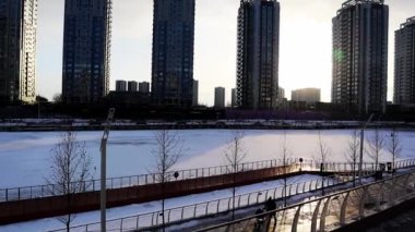 Kyiv, Ukrayna. 7 Aralık 2022 Çok katlı binalar yüksek evler. Toprak setin üzerinde yürüyen insanlar. Güzel kış günbatımı. Şehir manzarası ve sokaktaki insanların olduğu yavaş çekim videosu. Güneş batıyor