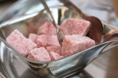 Rafine edilmemiş pembe şeker küpleri ve metal şeker maşaları kafede, restoranda, mutfakta gümüş şeker kasesinde servis ediliyor. Tatlı sağlıksız yemek. Yumuşak odak.