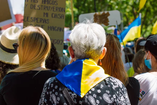 スペイン マドリード2022年5月1日ロシア戦争中のウクライナを支援する集会におけるスペイン人 抗議者の群衆 ウクライナの国旗の背景色の黄色の青の色のスカーフを持つ高齢者の女性 — ストック写真