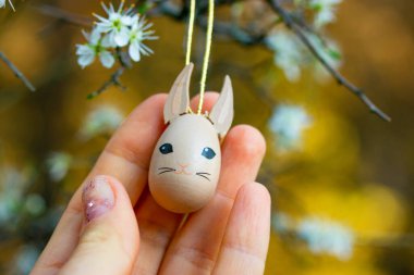 Kahverengi, komik, ahşap oyuncak kedi, kedicik, bir insanın elindeki kedi, çiçek açan bahar ağacına karşı. Süslü kolye, Paskalya tatili için süs. Bahar bahçesinde paskalya yumurtası. Şirin hayvan..