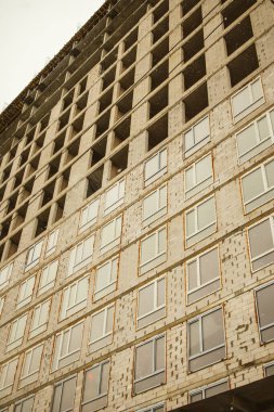 İnşaat alanının alçak açılı manzarasında, tamamlanmamış, yüksek katlı bir apartmanın tuğla cephesini cilalamak. Ev inşaatı, iş inşaatı. Penceresiz bir evin dış cephesi