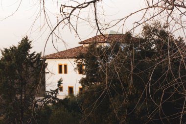 İki katlı beyaz bir kır evi çalılıkların arasında, ağaç dallarının arkasında. Gayrimenkul ile soyut bir özgeçmiş. Satın al, sat, kiralık evler villalar konsepti.