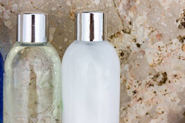 Seyahat konteynırlarında doğal kozmetik içeren plastik şişeler - beyaz duş jeli, içinde köpükler olan şampuan, kahverengi kaya zeminine karşı minyatür kaplarda vücut losyonu. Yüz bakımı. 