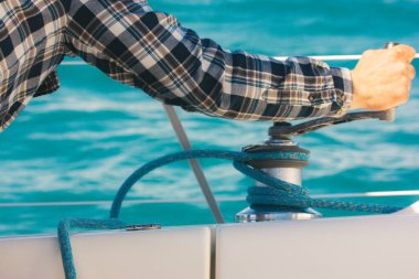 Yelkenli halatı vinçte çözüyorum. Denizcilerin ellerinin, mavi deniz suyuna karşı yelken ekipmanlarının detaylarını kapatın. Yaz günlerinde seyahat, yolculuk. Denizcilik yaşam tarzı. Denizci güvertesinde hareketlilik var..