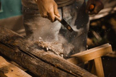 Çekiçle çalışan profesyonel bir marangoz. Farklı yönlere uçan tahta parçacıkları seçici odaklı sıkı çalışma süreci. Çok çalışkandır. Bir ev, bir tekne inşa etmek. İş gücü, iş gücü.