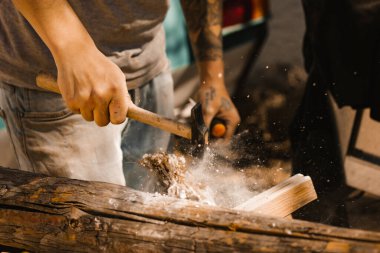 Çekiçle çalışan profesyonel bir marangoz. Farklı yönlere uçan tahta parçacıkları seçici odaklı sıkı çalışma süreci. Çok çalışkandır. Bir ev, bir tekne inşa etmek. İş gücü, iş gücü.