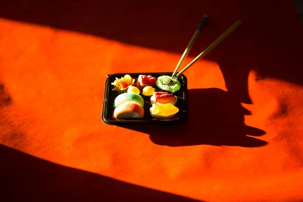 果冻糖果寿司设置在一个塑料黑色的盒子在明亮的红色背景对比黑暗的阴影 木制寿司用筷子把亚裔日本人的中国菜 糖果甜食 精美的食物照片 — 图库照片
