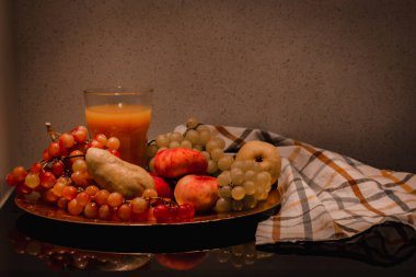 Meyve tabağıyla karanlık, sakin bir hayat. Mutfaktaki masada duran tabakta tropik çiğ meyveler. Bardakta taze meyve suyu. Yiyecek ve içecekler içeride..