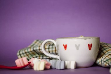 A cup of coffee, cocoa, chocolate with hearts on a lilac violet background. Marshmallows on a table. Cozy still life with hot drink made with love, sweets. February 14, Happy Valentines Day concept. 