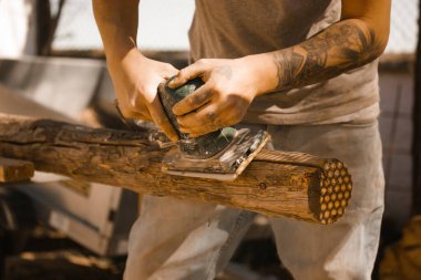 Sanatçının elleri ahşap kütüklerdeki eski cilalama makinesiyle kapanıyor. Özel bir marangozluk makinesiyle ahşap üzerinde çalışıyorum. Marangoz ya da mühendis ustası çok çalışıyor. Elektrikli cilalayıcı, Yörünge zımpara makinesi.