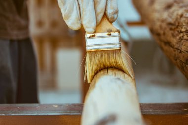 Yüzü olmayan usta bir marangoz, bir yüzeyi böceklerden korumak için tutkalla tedavi ederek ahşapla çalışır. Fırça tutan marangozluk işi. Tahtadan yapılmış ürünler. Ağaç kütükleri. Ahşap boyama, ahşap işçiliği.