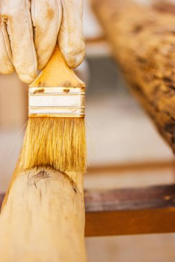 Yüzü olmayan usta bir marangoz, bir yüzeyi böceklerden korumak için tutkalla tedavi ederek ahşapla çalışır. Fırça tutan marangozluk işi. Tahtadan yapılmış ürünler. Ağaç kütükleri. Ahşap boyama, ahşap işçiliği.