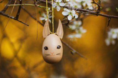Kahverengi sevimli oyuncak kedi, çiçek açan kiraz ağacının dalında kedi yavrusu. Paskalya kutlaması için dekoratif kolye, süs, dekor. Bahar bahçesinde dikey arka planda Paskalya yumurtası. Şirin hayvan.