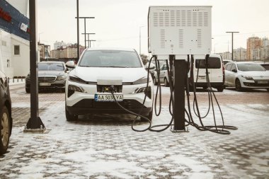 Kyiv, Ukrayna 2 Şubat 2023 Bir elektrik santralinde beyaz bir elektrikli araba şarj edilir. Kışın elektrik dolum istasyonunda ekolojik ulaşım. Şehir caddesinde arabalar için park yeri.