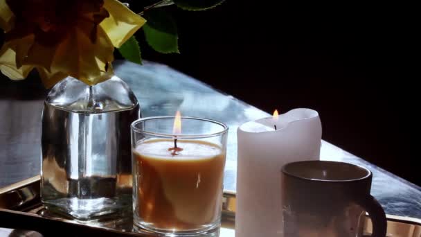 テーブルの上のテーブルの上に燃える炎を持つ2つの燃えるような香りのキャンドルは 暗い背景に1つの黄色のバラを持つ透明なガラス花瓶の近くにあります リラクゼーション 冷たい夜 スパのコンセプト花の静物画 — ストック動画