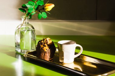 Bir fincan çay ya da altın tepside kahve, çikolatalı kek, mutfak masasında sarı bir gül olan cam bir vazo. Romantik kahvaltı. Güneş ışığında yiyecek ve içecek. Tatlı fırın.