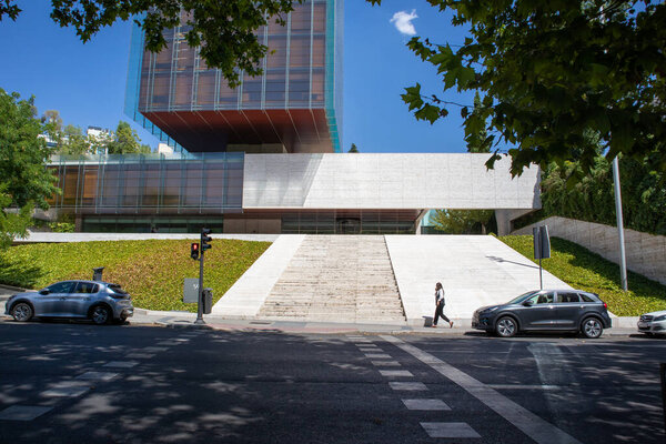 Мадрид, Испания. 1 июля 2022 года Городская сцена Люди, идущие по улице Машины припаркованы на дороге. Современное здание со стеклянным фасадом. Офисное здание города. Бизнес и финансовый центр. Современная архитектура и строительство.