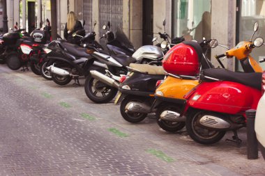 Madrid, İspanya. 1 Mayıs 2022 Çok renkli kırmızı ve turuncu scooter 'lar, eski bir caddede arka arkaya park edilmiş motosikletler. Bisikletler için park yeri. Ekolojik araç, klasik motosikletler. Şehir hayatı.