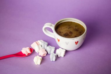 A cup of coffee, cocoa, chocolate with hearts on a lilac violet background. Marshmallows on a table. Cozy still life with hot drink made with love, sweets. February 14, Happy Valentines Day concept. 