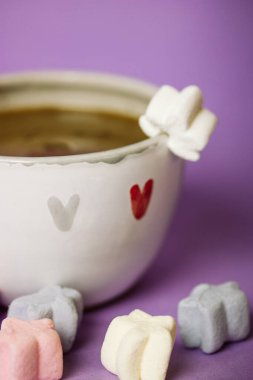 A cup of coffee, cocoa, chocolate with hearts on a lilac violet background. Marshmallows on a table. Cozy still life with hot drink made with love, sweets. February 14, Happy Valentines Day concept. 