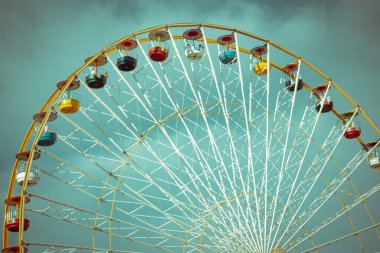 Mavi arka planda şeffaf kabinleri olan beyaz bir dönme dolap. Şehir eğlencesi. Luna park oyunları, çocuklar için eğlence, atlı karınca. Aşağıdan yüksek inşaat manzarası. Kumarbazlar için bir cazibe.. 