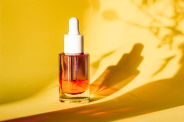 Sarı arka planda yüz ve vücut bakımı için serumu olan cam kozmetik kavanozu. Kadınlar için bakım ürünleri. Kadın güzellik aleti ve kozmetik. Bitkilerin gölgeleriyle doğal arkaplanda yüz serumu.