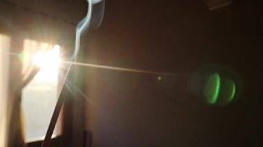 Tütsü kokulu çubuk sigara dumanı pencerenin arka planına karşı güneş ışığında duman çıkarıyor. Evde hoş bir koku için tütsü. Sabah güneşinde evde meditasyon. Budizm.