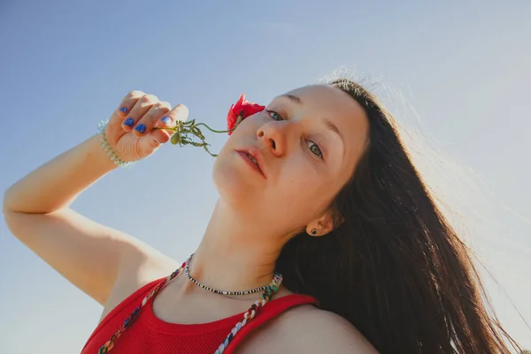 Elinde Kırmızı Gelincik Çiçeğiyle Mavi Gökyüzüne Bakan Esmer Bir Kadın — Stok fotoğraf