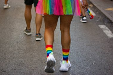 Madrid, Spain. July, 25, 2022 Man wearing rainbow-colored skirt, socks in LGBT colors walks city street at Gay parade, festival, event in Pride month. Hairy male legs rear back view. People have fun.