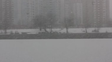 Göle düşen kar taneleri, soğuk havada akan nehir. Buz gibi bir günde kar taneleri yere düşüyor. Bir şehirde karlı bir gün, ufukta konut binaları, soğuk kış mevsimi. 