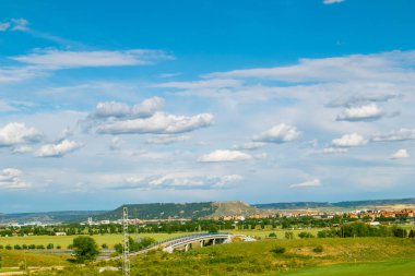 Baharda bulutlu mavi gökyüzüne karşı ufukta yeşil ağaçların olduğu güzel bir manzara. Tarlalar, çayırlar, araziler, köyler. Hava çok güzel. Doğa manzarası. Sakinlik, uyum kavramı