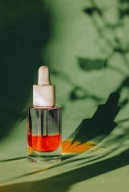 Yeşil arkaplanda kırmızı yüz serumu kavanozu ve bitki kontrastı gölge deseni. Vücut bakımı için kozmetik ürünleri. Kütikül yağı. Pipetli kozmetik şişesi. Günlük rutin. Şık kozmetik ürünler.