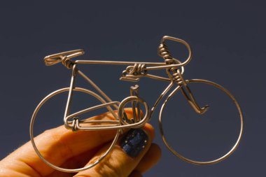 A metal bicycle in a woman's hand against a dark blue-gray sky. Holding a toy mini bike. Cycling in mountains. Round aluminum wheels of a bike. Healthy lifestyle, outdoor leisure and sports concept.