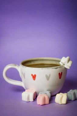 A cup of coffee, cocoa, chocolate with hearts on a lilac violet background. Marshmallows on a table. Cozy still life with hot drink made with love, sweets. February 14, Happy Valentines Day concept. 