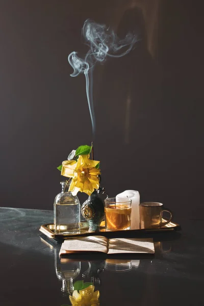 暗い垂直静物茶コーヒーカップ 黄色のバラの花が咲き 春に花瓶に花を咲かせ 開いて本はテーブルの上に横たわる 家の装飾パロサント香煙のパフが立ち上がる香りスティック — ストック写真