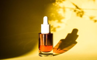 Sarı arka planda yüz ve vücut bakımı için serumu olan cam kozmetik kavanozu. Kadınlar için bakım ürünleri. Kadın güzellik aleti ve kozmetik. Bitkilerin gölgeleriyle doğal arkaplanda yüz serumu.