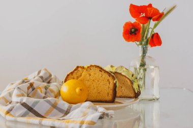 Kırsal yaşam, cam vazoda kırmızı haşhaş ve mutfak masasında biscocho Bizcocho limonlu kek. Evde hazırlanmış tatlı. Kırmızı bir fincan kahve ya da çay. Bisküvi pastaları, kekler.. 