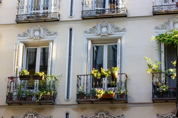 Old white building facade with beautiful open balconies decorated with flower pots. Growing flowers and plants at home. Old European street Residential building, Mediterranean classical architecture