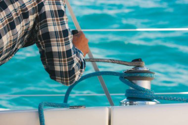 Yelkenli halatı vinçte çözüyorum. Denizcilerin ellerinin, mavi deniz suyuna karşı yelken ekipmanlarının detaylarını kapatın. Yaz günlerinde seyahat, yolculuk. Denizcilik yaşam tarzı. Denizci güvertesinde hareketlilik var..